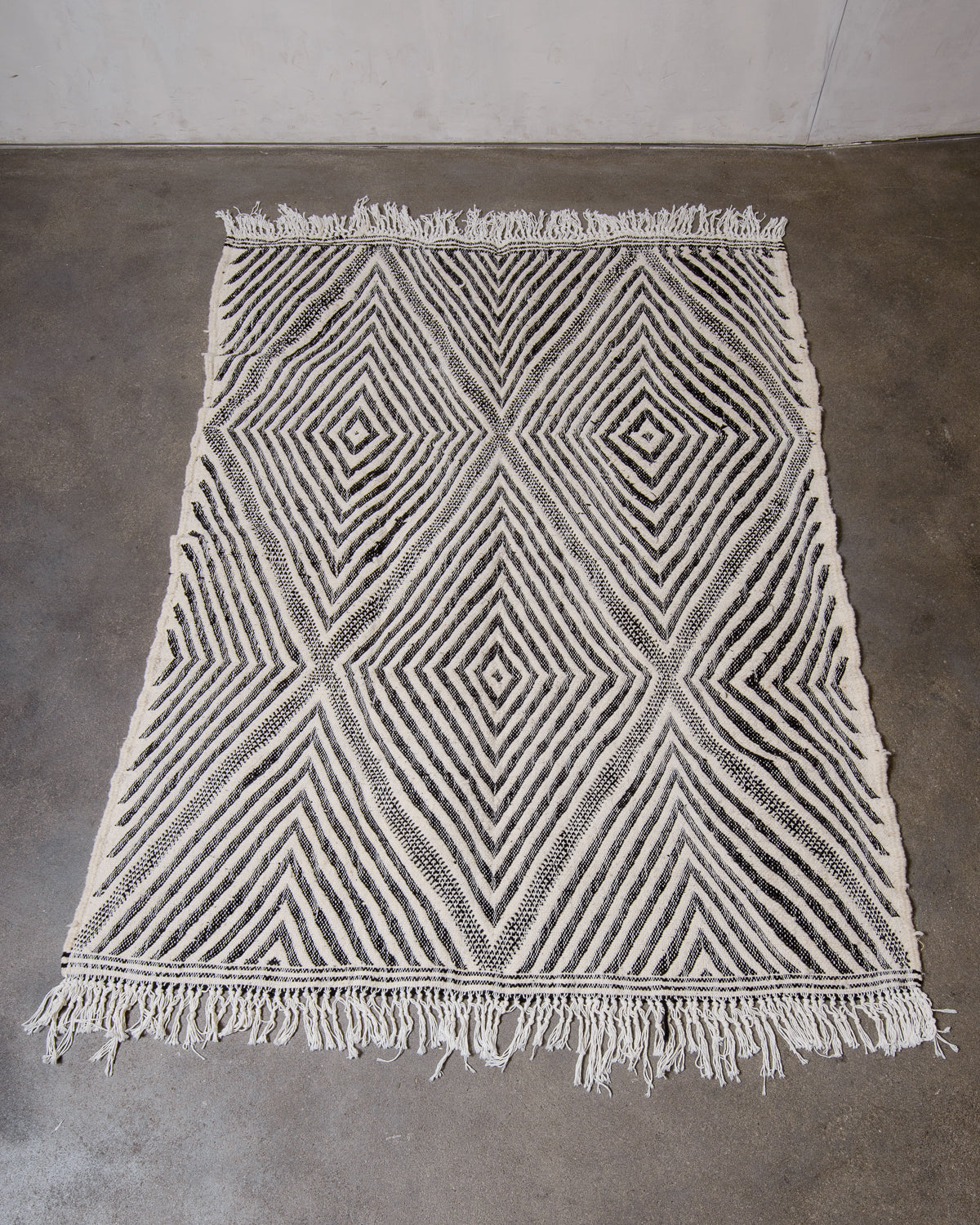 Black and white Kelim rug from Morocco laying on concrete floor.